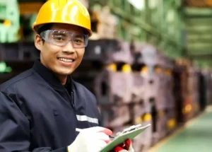 An asian worker holding a clipboard in a factory.