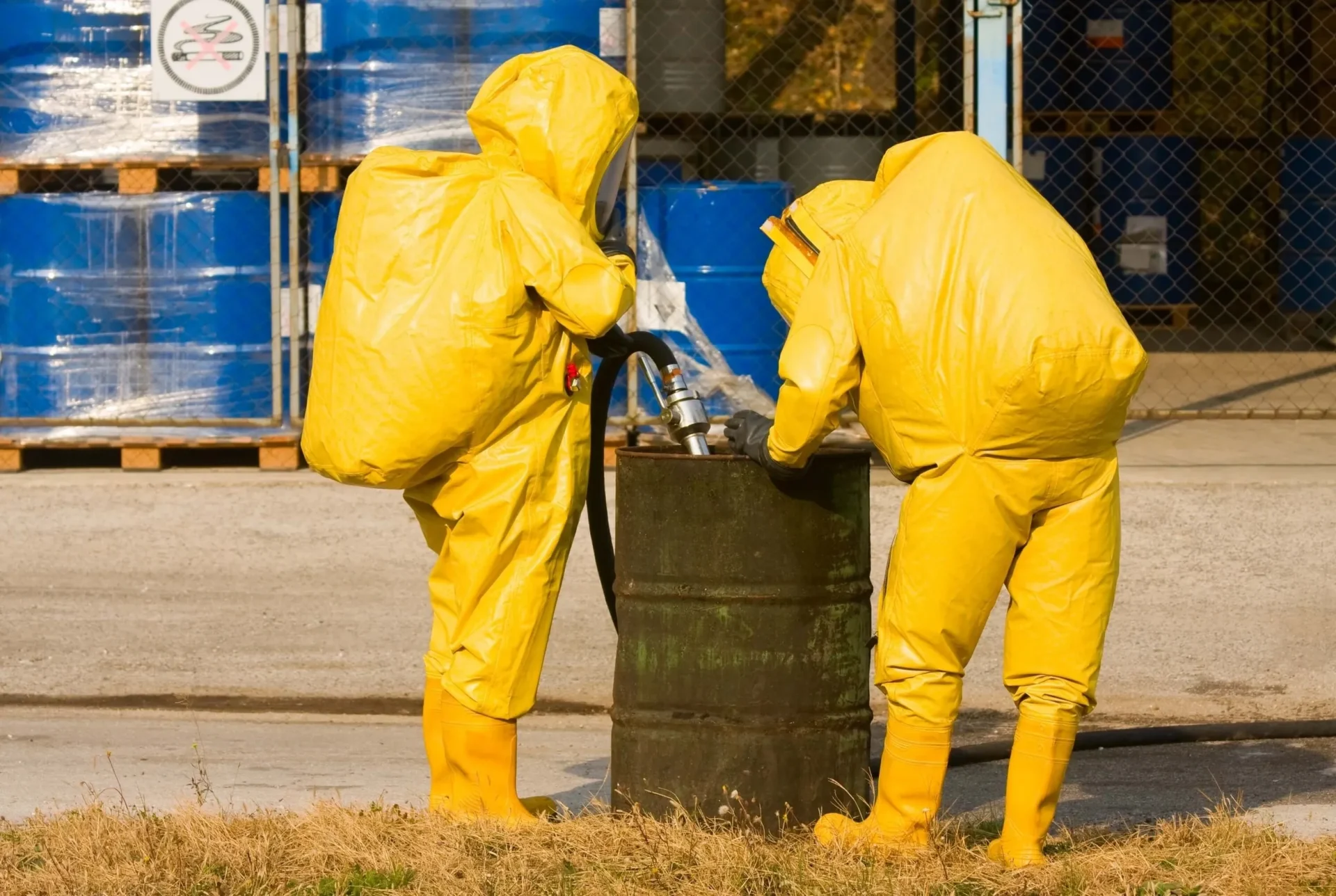 Two people in yellow protective suits standing next to a barrel.